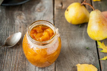 Close up Pear jam and fresh yellow ripe pears on old rustic wooden table. Autumn harvest still life concept. Selective focus. Space for text