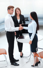 business partners shaking hands while standing in the lobby of the office.