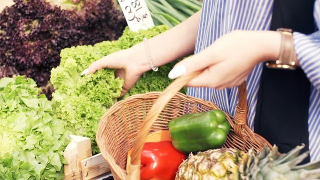 Woman hand add fresh lettuce to the basket at a local farmer`s market
