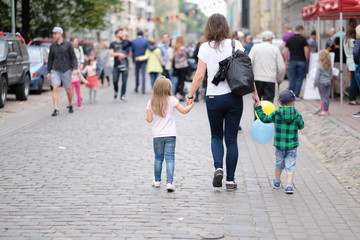 Children go with their mother along the street, holding their hands on the city holiday. Riga, Latvia.