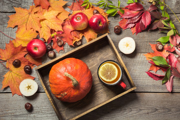 Warming cup of tea with a decor of pumpkins and autumn leaves on a wooden vintage board.