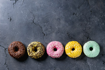 Variety of colorful glazed donuts over black texture background. Top view with space