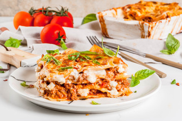Italian food recipe. Dinner with classic lasagna bolognese with béchamel sauce, parmesan cheese, basil and tomatoes, on white marble table, coopy space - obrazy, fototapety, plakaty