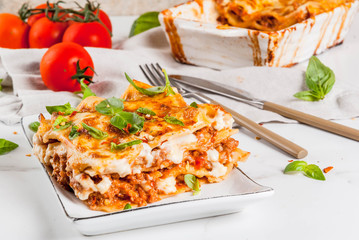 Italian food recipe. Dinner with classic lasagna bolognese with béchamel sauce, parmesan cheese, basil and tomatoes, on white marble table, coopy space