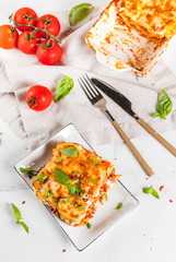 Italian food recipe. Dinner with classic lasagna bolognese with béchamel sauce, parmesan cheese, basil and tomatoes, on white marble table, coopy space