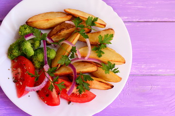 Roasted potato slices, cooked broccoli, fresh tomatoes with spices, red onion, parsley leaves on a white plate and on a purple wooden background. Easy vegan dish. Top view