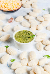 Raw uncooked homemade potato gnocchi with flour, grated parmesan cheese, basil and pesto sauce. On concrete light blue background, copy space