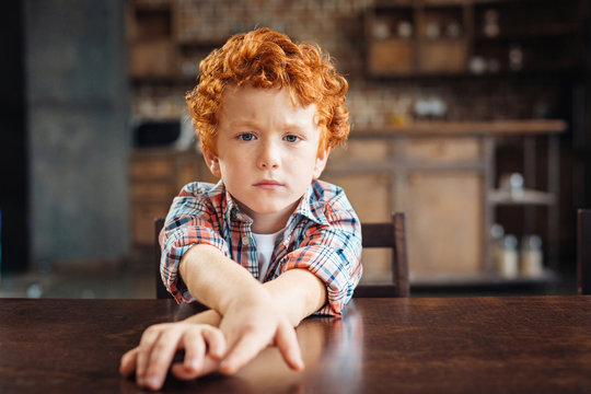 Bored redhead little boy sitting at table
