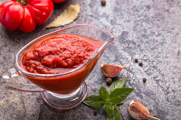 Tomato ketchup sauce with garlic and  basil  in gravy boat on stone background,  copy space