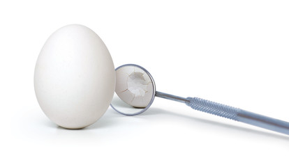 Broken egg with dental mirror on white background. Creative idea