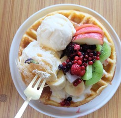 Dessert with waffles ,fruit and ice cream in a plate on a wooden table.