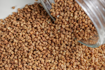 Uncooked buckwheat scattered from jar on table