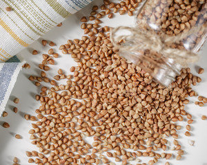 Uncooked buckwheat scattered from jar on table