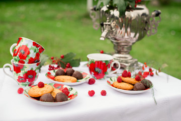 Самовар с чашками и десертом с малиной на столе в саду. Завтрак на природе 