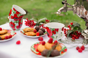 Самовар с чашками и десертом с малиной на столе в саду. Завтрак на природе 