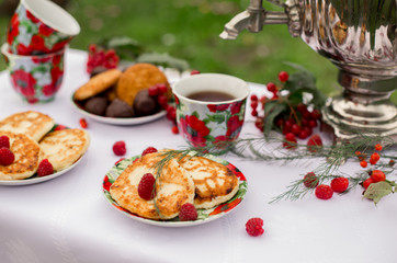 Obraz na płótnie Canvas Самовар с чашками и десертом с малиной на столе в саду. Завтрак на природе 