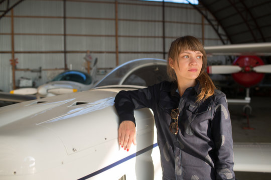 Young female pilot standing in hangar besides the airplane