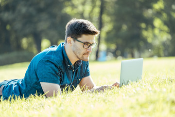 Young man lying on grass and using laptop