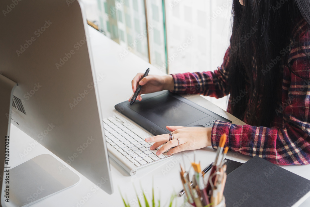 Poster young asian female designer using graphics tablet while working with computer at studio or office.