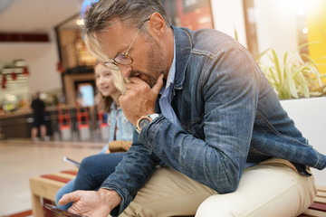 Fototapeta premium Man sitting on public bench in shopping mall