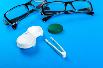Fototapeta na wymiar glasses, contact lenses in containers and tweezers on blue background