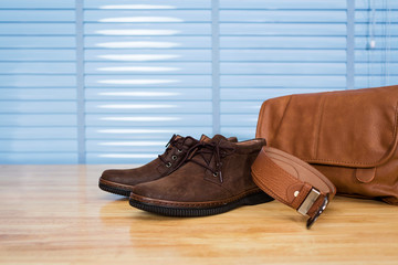 Men's leather fashion clothing, shoes, bag and belt on plywood table desk in business office room.