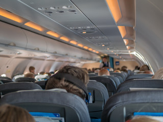 Airplane cabin interior with grey seats, passengers and soft lightning.