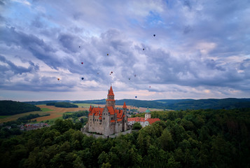 Aerial view on romantic fairytale castle Bouzov with hot air balloons against dramatic sky in picturesque czech landscape. Hot air balloon festival, Bouzov castle, Moravia, Czech republic.