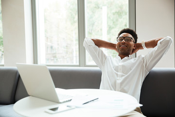 Cheerful young african man sitting coworking by laptop