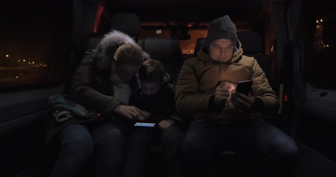 Three passengers traveling by minibus in late evening. Mother and son entertaining with smart phone and man passing the time with browsing on mobile