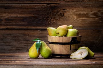 fresh pears with leaves in a basket on wooden background