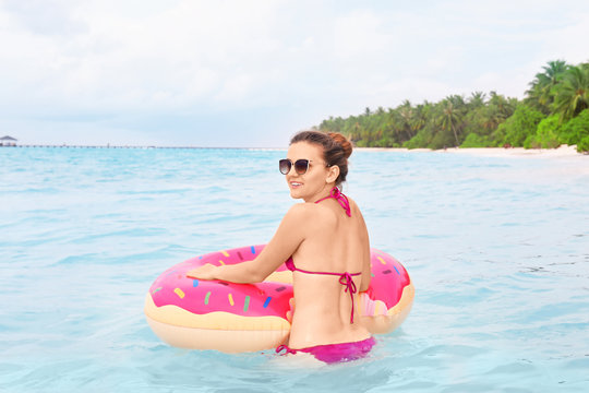 Beautiful young woman bathing with colorful inflatable donut at resort