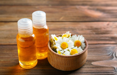 Bottles of essential oil and chamomile flowers on wooden table
