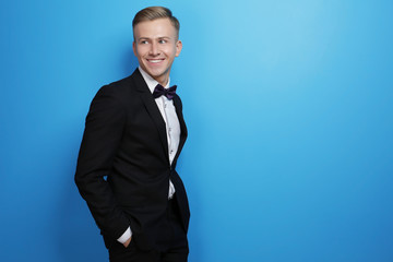 Handsome man in elegant suit on color background