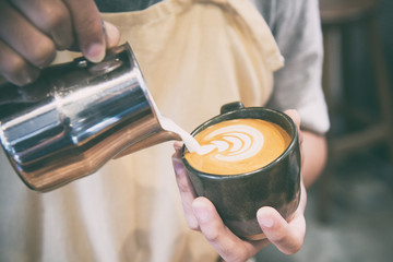 hand of barista making latte or cappuccino coffee pouring milk making latte art