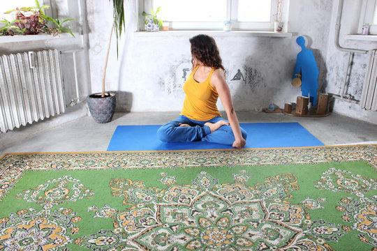 Young attractive smiling woman practicing yoga, sitting in One Legged King Pigeon exercise, Eka Pada Rajakapotasana pose, working out, wearing sportswear, grey pants, bra, indoor full length, home