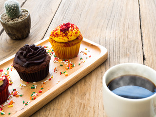 Yellow and chocolate cupcakes put on a spherical wooden plate. Beside of cupcake have Cactus and white coffee mug.All of it rests on wooden table.