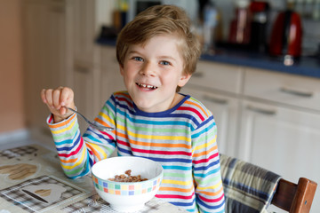 Happy little blond kid boy eating cereals for breakfast or lunch. Healthy eating for children.