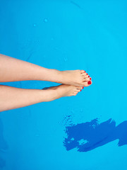 Fototapeta na wymiar Woman's feet with red nails on the swimming pool