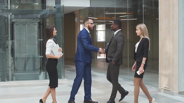 Young business team meet and shake hands in the lobby of a busy modern office building.