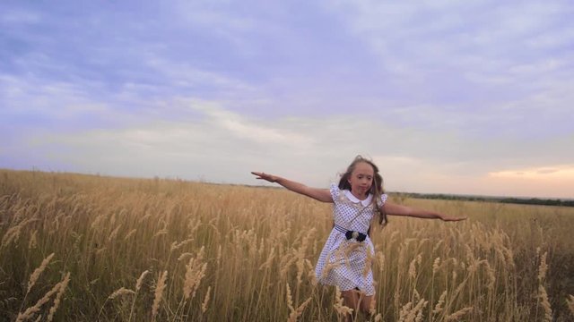 Girl teenager spread out her arms like wings and runs across field against blue sky smiling. Slow motion.