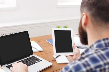 Young casual manager working with laptop and tablet in office, close up