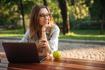 Smiling brunette woman in eyeglasses sitting by table