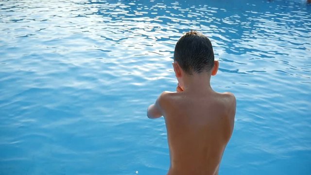 A seven-year-old courageous boy jumps feet first into the sea water on a sunny day in summer in slow motion. The playful sea waters look picturesque and wonderful 