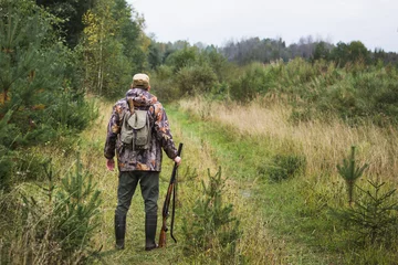 Deurstickers Jacht Jager met een rugzak en een jachtgeweer in het herfstbos. De man is op jacht. Achteraanzicht.
