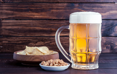 glass of cold frothy lager beer and snacks on wooden table