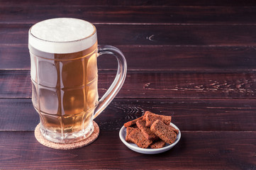 glass of cold frothy lager beer and plate of snacks on wooden table