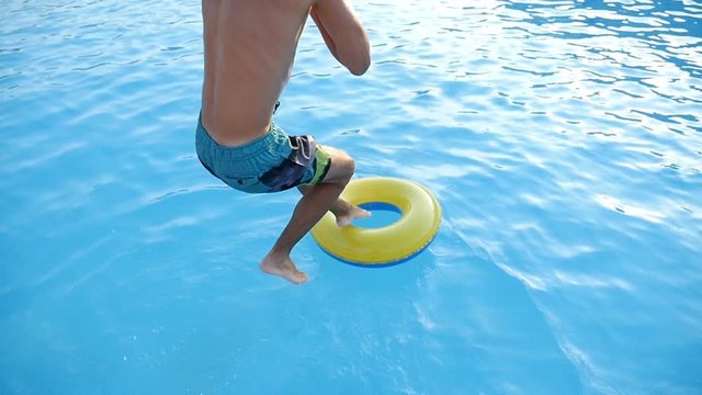 Young sportive man jumps into a yellow and blue  inflatable ring into the sea feet first in summer in slow motion. The seascape with playful waters look gorgeous