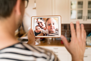 Father at home with tablet, video chatting with his family.