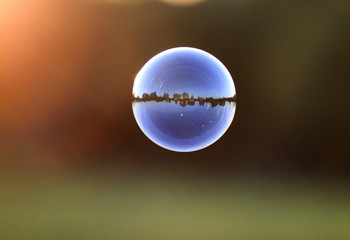 beautiful iridescent soap bubble with reflection landscape flies by sundown
